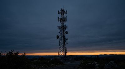 A cellular tower silhouetted from below against a deep slate dusk sky with a narrow amber band at the horizon.
