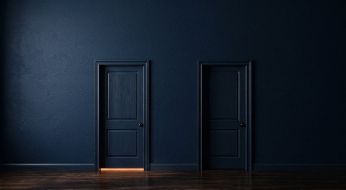 Two identical closed doors, warm amber light showing at the gap beneath the left one and none beneath the right.