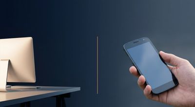 A split view of a bright desktop monitor on one side and a hand holding an older Android phone on the other.